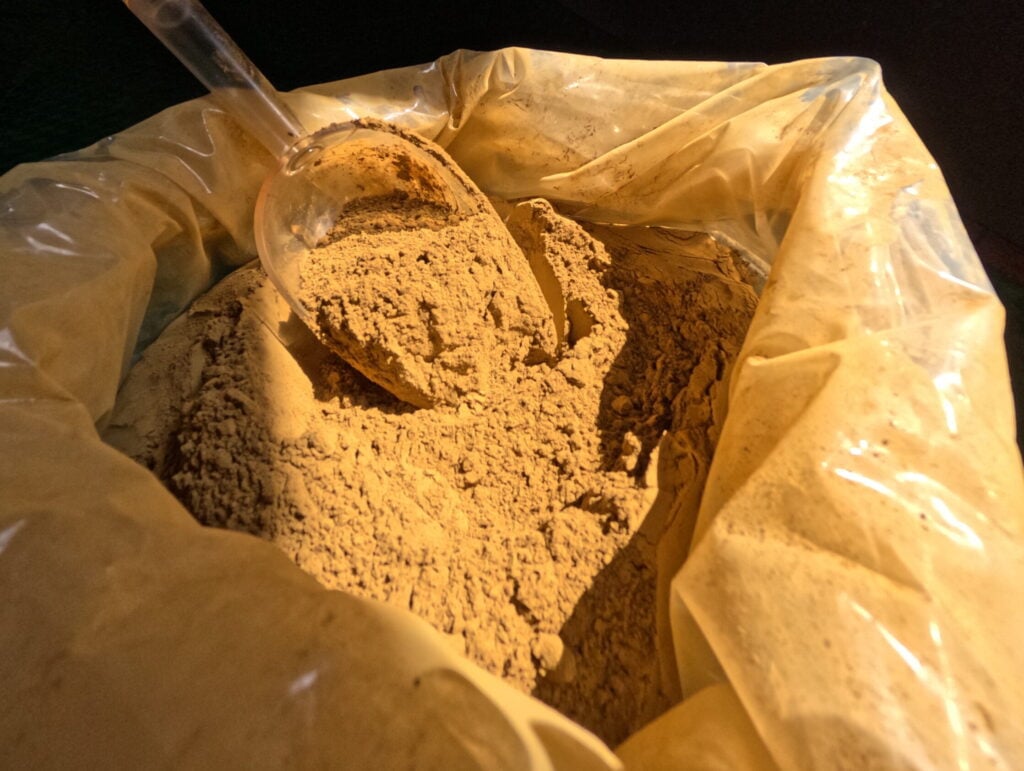 Red kratom powder in a plastic bag, dark background
